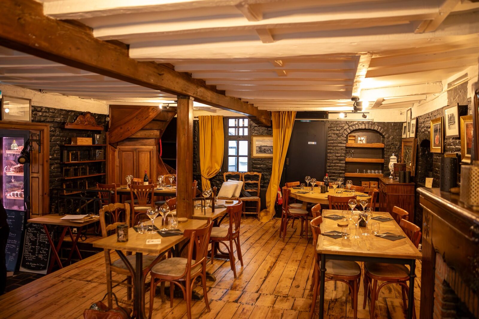 La salle de L'Auberge de Mouvaux : poutres blanches, briques noires et rideaux jaune moutarde